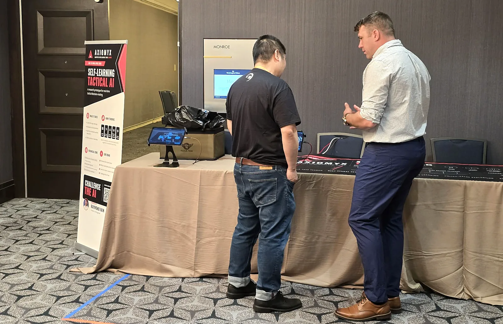 Raymond Fain talking a player through a move at the Axiomyx demonstration table at Nova Open 2026.